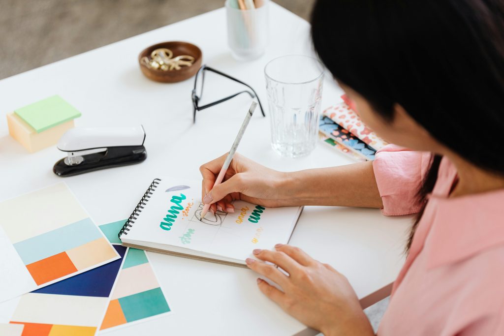 Woman at desk with color swatches, notpad and eyeglasses, working on a creative project.