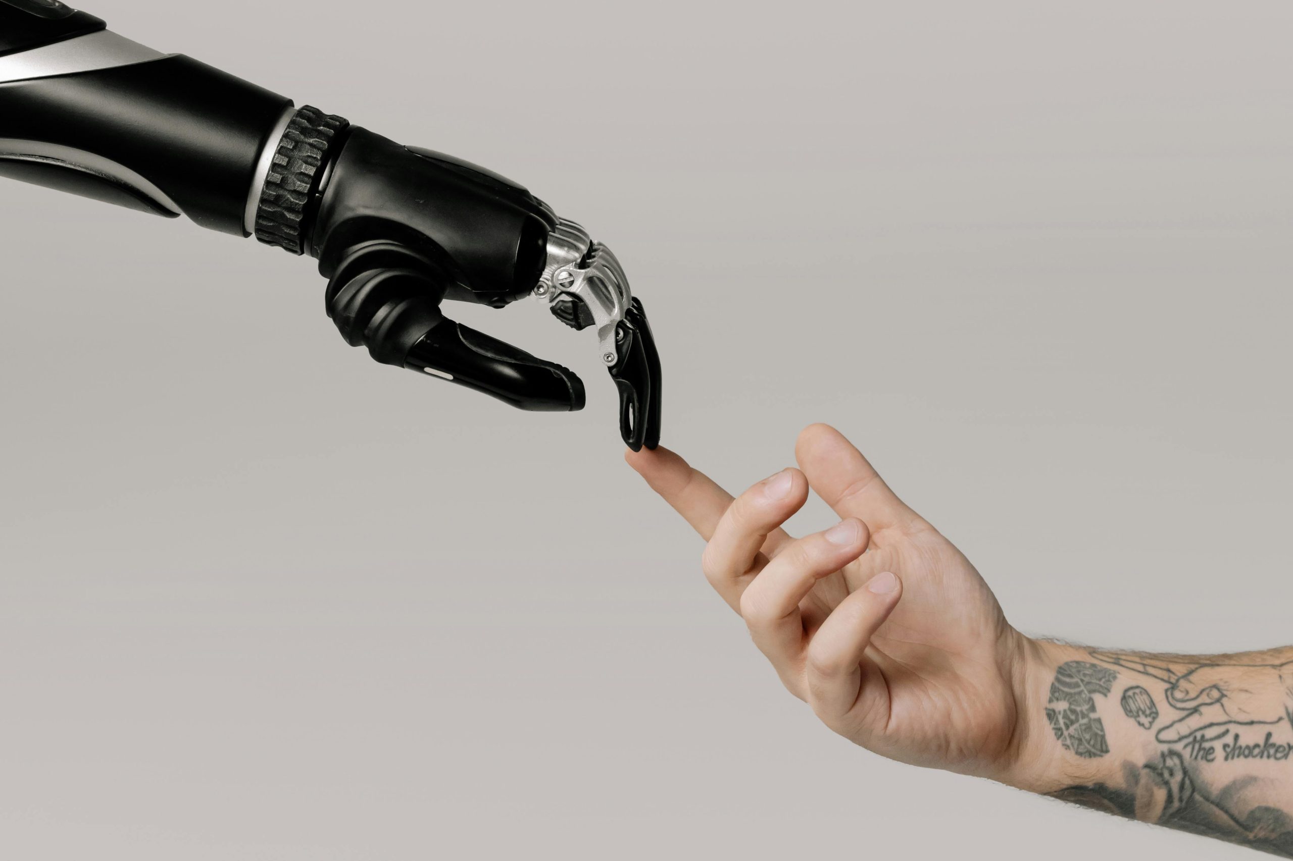 A robotic hand gently touching a tattooed human finger, symbolizing the connection between technology and creativity in modern workflows and Automating Admins.