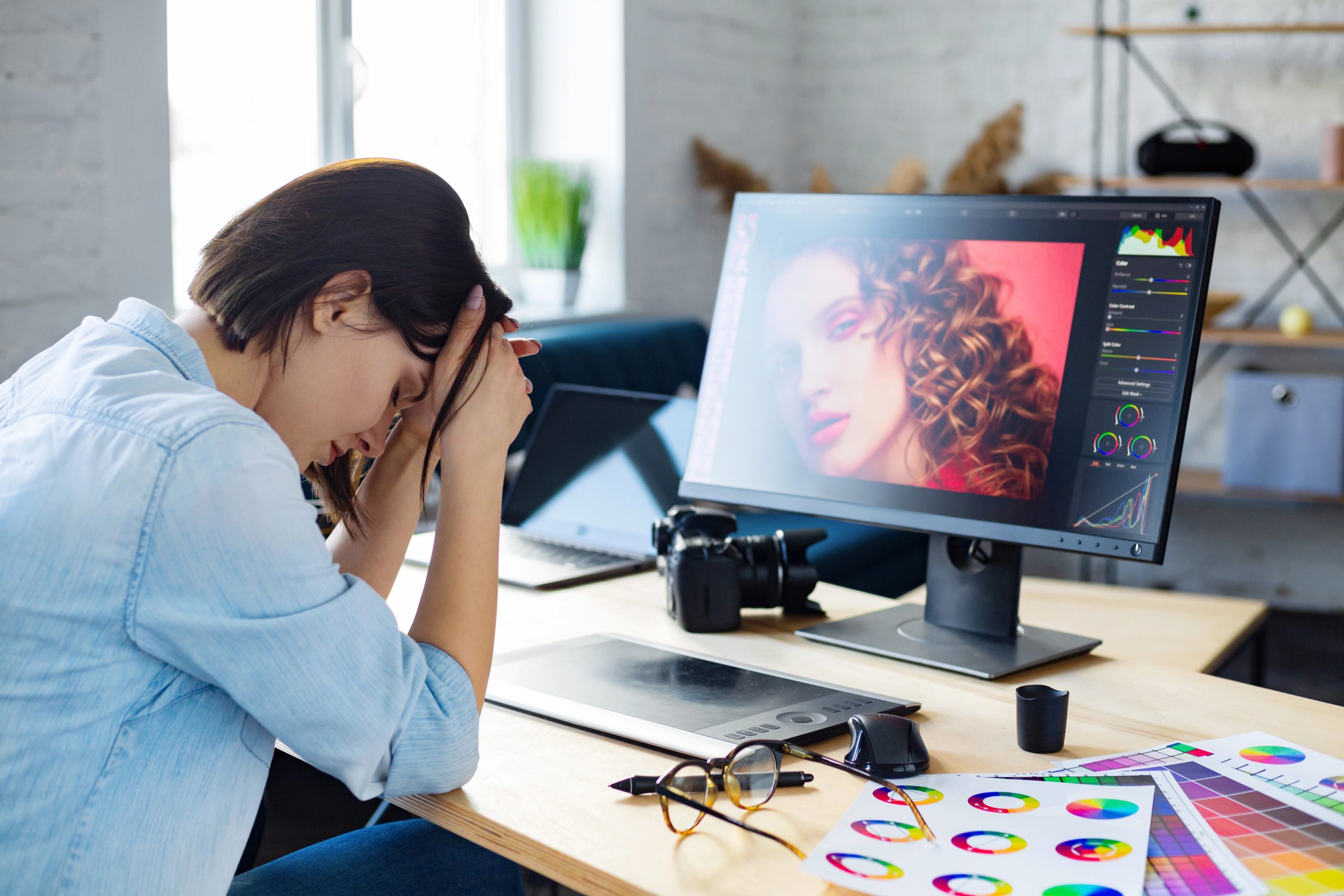 Tired graphic designer working overtime, showing early signs of financial red flags while retouching a photo in her office.