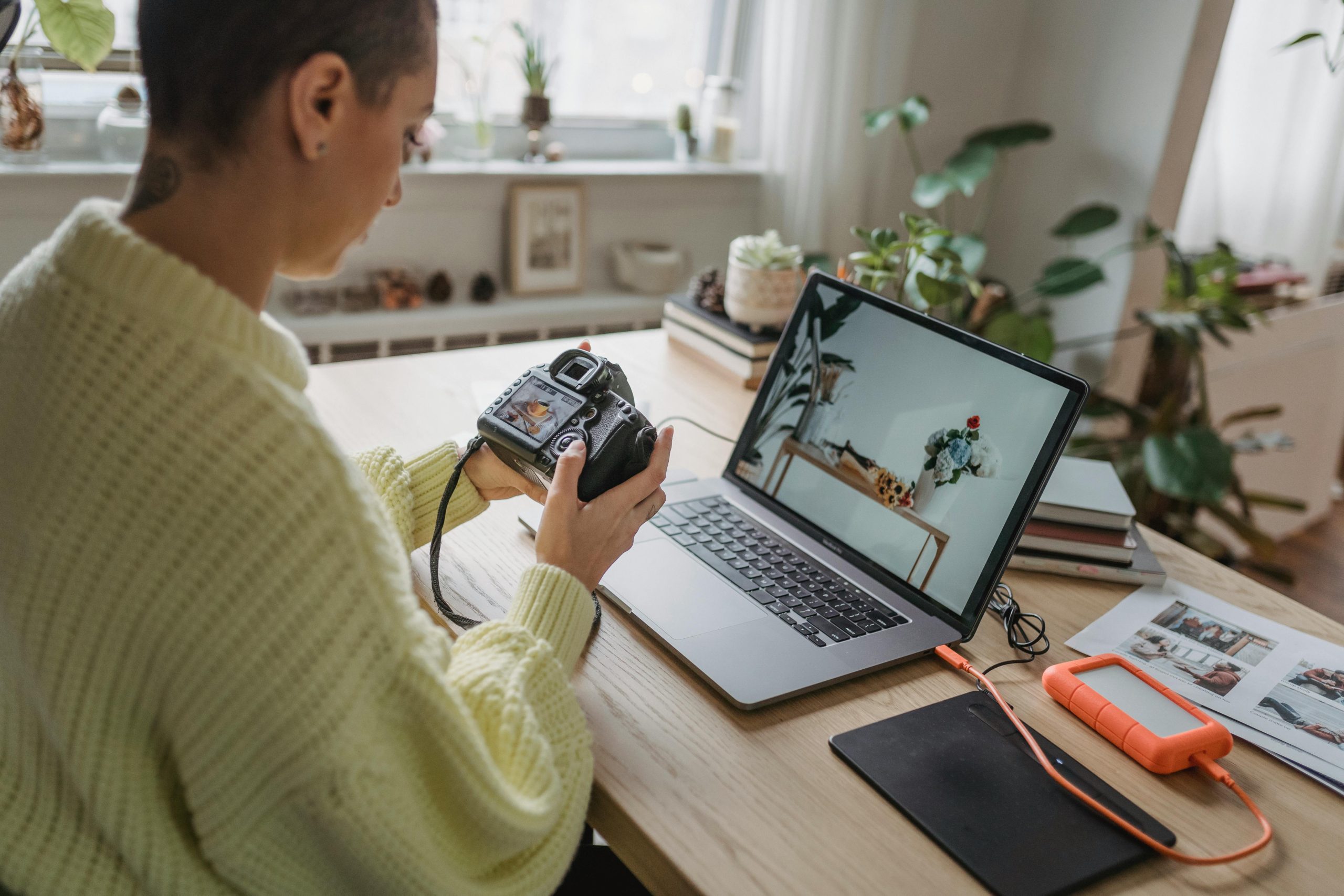 Creative professional reviewing work at her desk with a laptop and camera, representing the impact of underbilling your time.