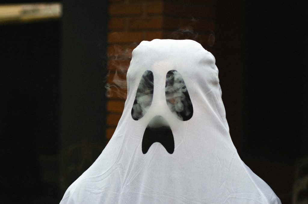 : Person wearing a white sheet ghost costume with blacked out eyes and mouth, symbolizing a client ghosting after receiving an invoice