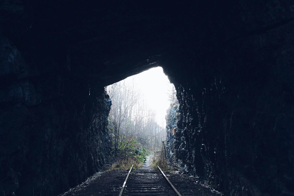 Railroad tracks leading from a dark tunnel into bright daylight, symbolizing breaking the feast-or-famine cycle for creatives.