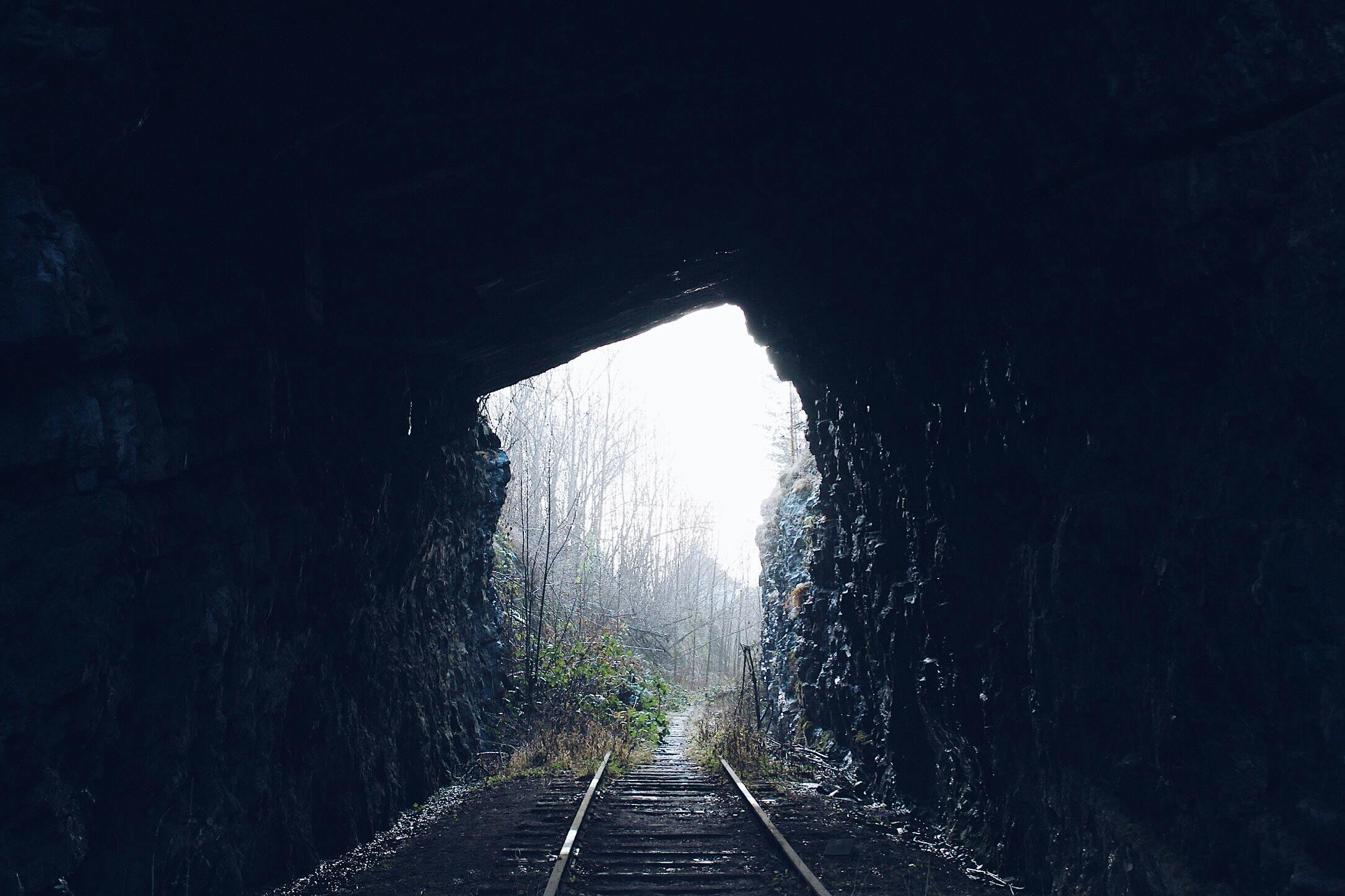 Railroad tracks leading from a dark tunnel into bright daylight, symbolizing breaking the feast-or-famine cycle for creatives.