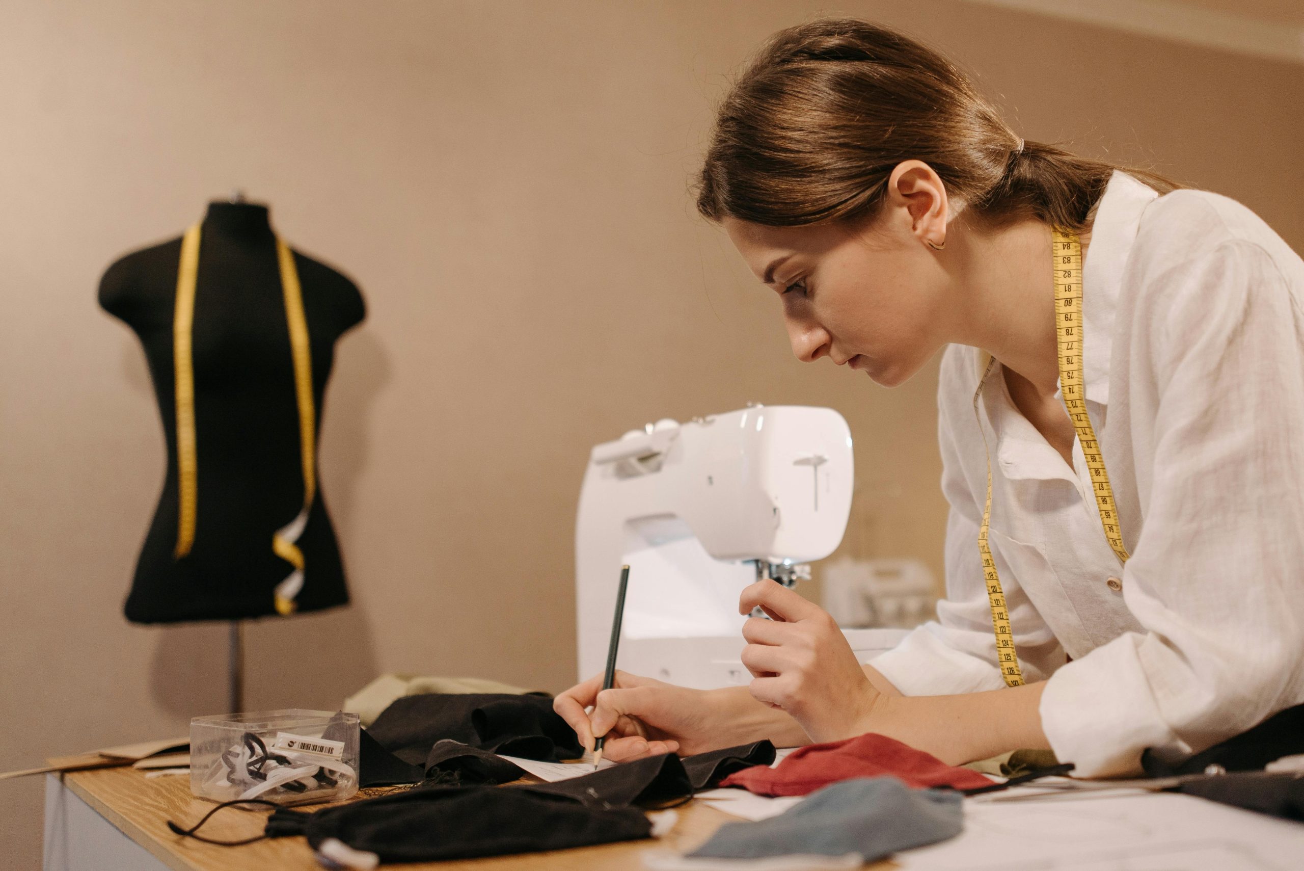 Fashion designer working in an atelier studio with fabric and sewing machine, symbolizing focus and creativity balanced with bookkeeping systems.